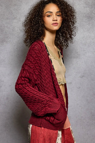 Open front cardigan in oxblood with a cable knit design worn by a model.