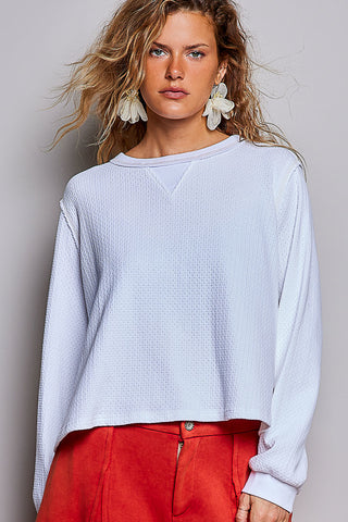 A woman wearing an oversized waffle knit long sleeve top in off white.