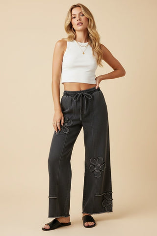 Black wide leg denim pants with floral appliqué and elastic drawstring waist.