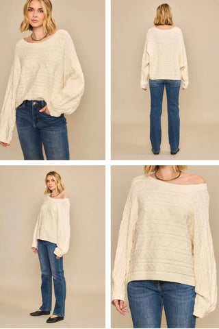 Off white sweater with horizontal cable knit, wide boat neckline, and dolman sleeves worn by a model with jeans.