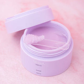 Lavender-colored makeup removing balm in a round lavender container with a small applicator scoop.