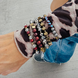 A stack of multicolor beaded bracelets with metallic accents on a wrist, styled with a patterned sleeve.
