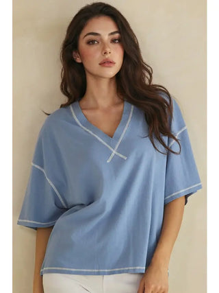 A woman wearing a denim white V-neck top with contrast stitching.
