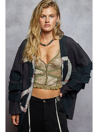 Navy cardigan with V-neck, peace patch, and ruffle details worn by a model.