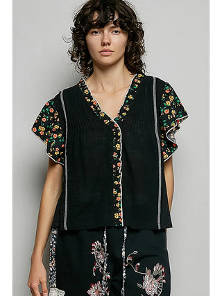 A black V-neck top with ruffle sleeves, pintuck detailing, and floral woven accents.