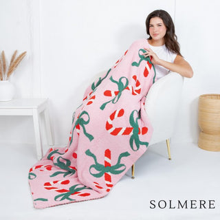 Pink blanket with a candy cane and green bow pattern, draped over a chair.