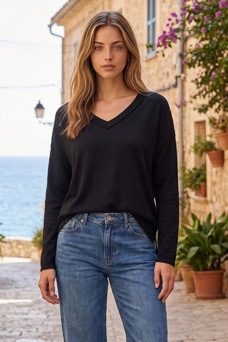A woman wearing a black long-sleeve V-neck top with jeans, standing outdoors.