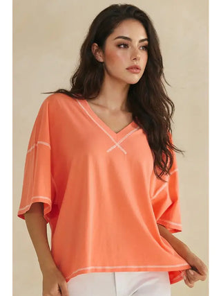A coral V-neck top with white contrast stitching and short sleeves worn by a model.