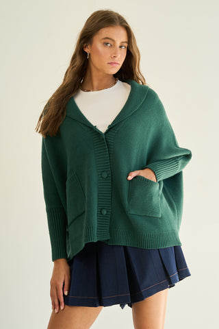 A green oversized shawl collar sweater cardigan with button front and pockets.