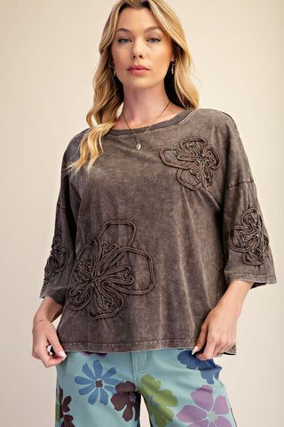 A woman wearing a mocha terry top with floral embroidery and half-length sleeves.
