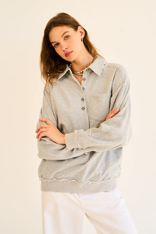A woman wearing a heather grey polo sweatshirt with a buttoned front and a structured collar.