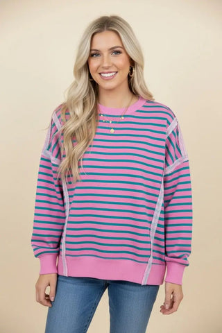 A woman wearing a pink and teal striped oversized sweatshirt with exposed seams.