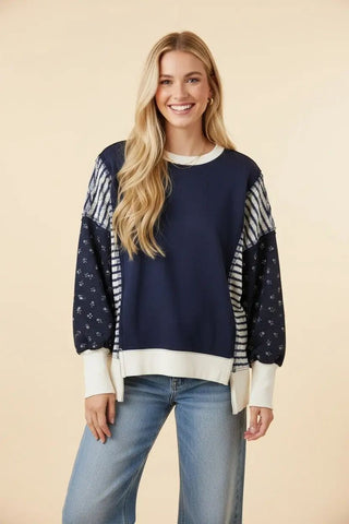 A woman wearing a navy oversized knit sweatshirt with mixed prints and light blue jeans.