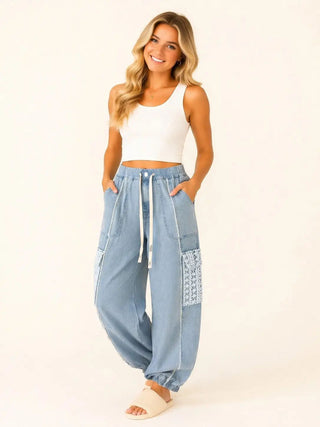 Woman wearing denim jogger pants with lace pocket details and a drawstring waist.