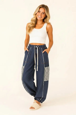 Woman wearing dark denim jogger pants with lace pockets and a drawstring waist.