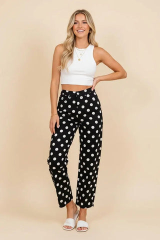 Model wearing black and white polka dot high rise straight leg pants paired with a white top.