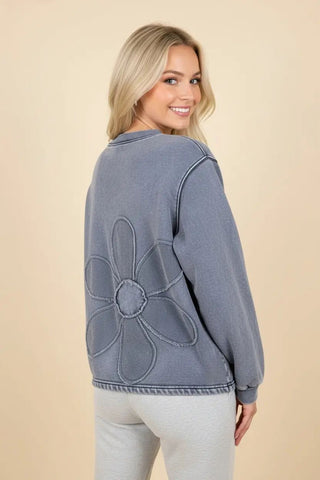 A model wearing a denim-colored oversized sweatshirt with a large floral stitch detail on the back.