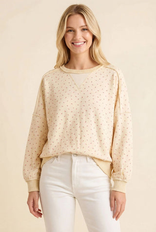 Ivory sweatshirt with an allover floral print and crew neckline, worn by a smiling person.
