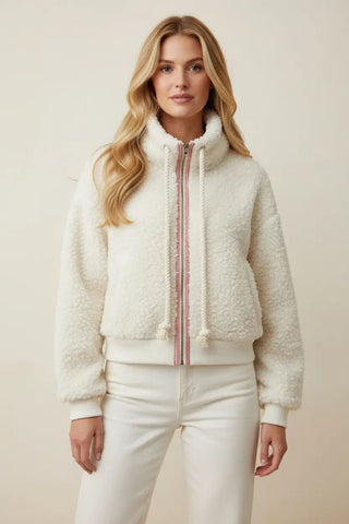 A woman wearing an ivory and red zip front mock neck Sherpa fleece jacket with a drawstring detail.