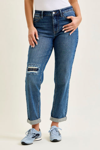 Pair of medium blue boyfriend jeans with embroidered repair patch, worn by a model.