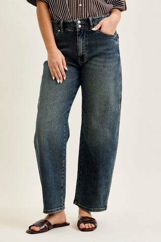 High waist jeans in medium denim with double button closure, worn by a person standing with hands in pockets.