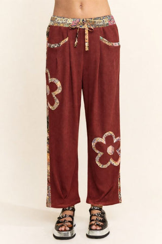 Burgundy waffle knit pants with paisley patchwork design, featuring a drawstring waist and floral patterns.