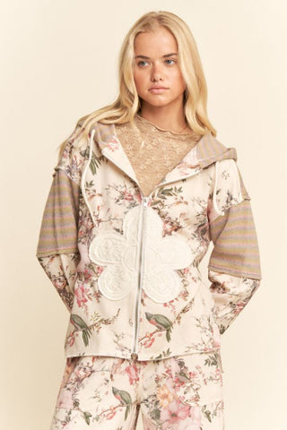 A model wearing a cream sage floral patchwork zip-up hooded jacket with an attached hood.