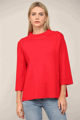 A woman wearing a red mock neck sweater with bell sleeves and a relaxed fit.