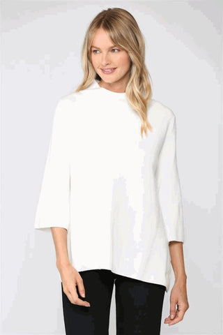 A woman wearing a cream mock neck pullover sweater with bell sleeves.