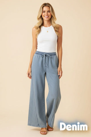 A model wearing wide leg denim pants in a light blue shade, paired with a white tank top.