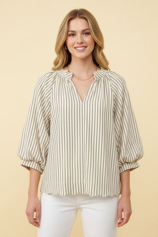 A woman wearing a cream blouse with vertical stripes and three-quarter sleeves.