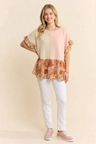 A woman wearing a peach orange top with a floral chiffon hem and ruffle trim.