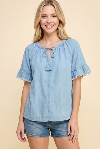 Light denim chambray blouse with tassel tie neckline and short ruffled sleeves.