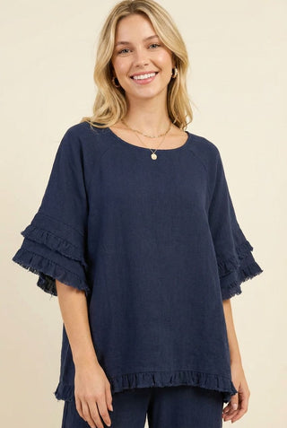 A woman wearing a navy blouse with ruffle sleeves and tiered trim.