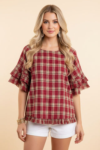 A woman wearing a red plaid blouse with ruffle sleeves and a relaxed fit.