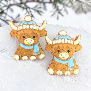 Two brown cow-shaped vent clips and magnets with blue hats and scarves on snowy background.