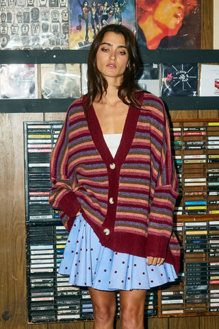 A woman wearing a wine multi-stripe oversized sweater cardigan with buttons.