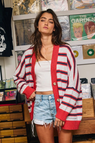 A woman wearing an oversized cardigan with oatmeal and red stripes, featuring a button front.