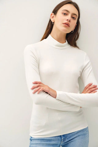 A woman wearing a long-sleeve ivory mock neck top with a fitted silhouette.