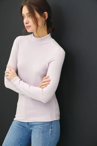 A woman wearing a pale rose mock neck long-sleeve top with blue jeans.