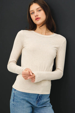 Model wearing an oatmeal-colored long sleeve knit top with a round neckline.