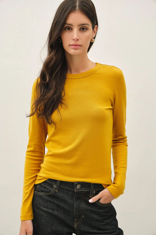 A woman wearing a dijon colored knit top with a round neckline and long sleeves.