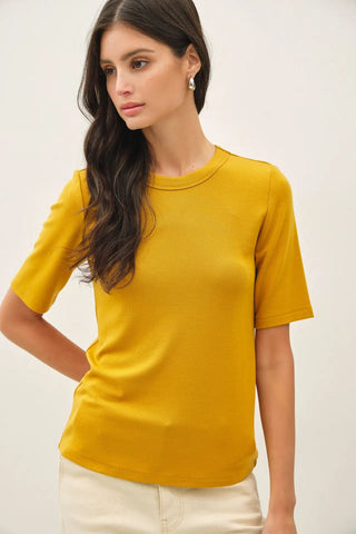 A woman wearing a dijon-colored short sleeve top.