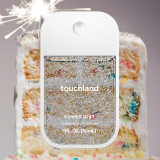 Touchland Power Mist hand sanitizer with confetti cake fragrance, 1 fl. oz., in a compact spray bottle next to a slice of confetti cake.
