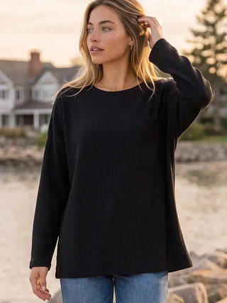A woman wearing a black ribbed long sleeve crew neck top with a relaxed fit.