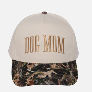 A cream baseball cap with 'Dog Mom' embroidered in the front, featuring a camo-patterned brim.