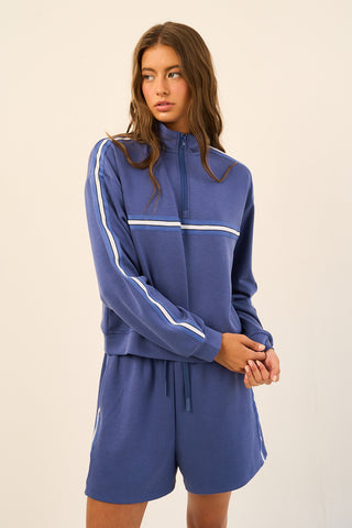 Woman wearing a classic blue lounge set with a zip-up top and stripe details on sleeves