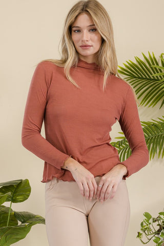 A woman wearing a rust-colored ribbed long sleeve top with lettuce trims.