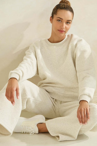 A woman wearing a heather grey oversized fleece sweatshirt, sitting in a relaxed pose.