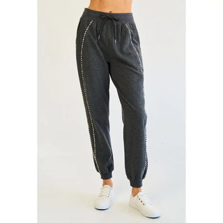 Charcoal jogger pants with piping detail and elastic waistband shown on a model wearing white sneakers.